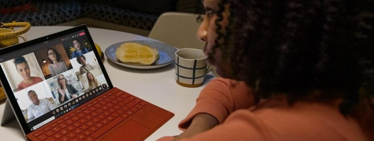 Une femme assise à une table avec un café participe à une rencontre de groupe sur son ordinateur. Les autres participants sont en vidéos.