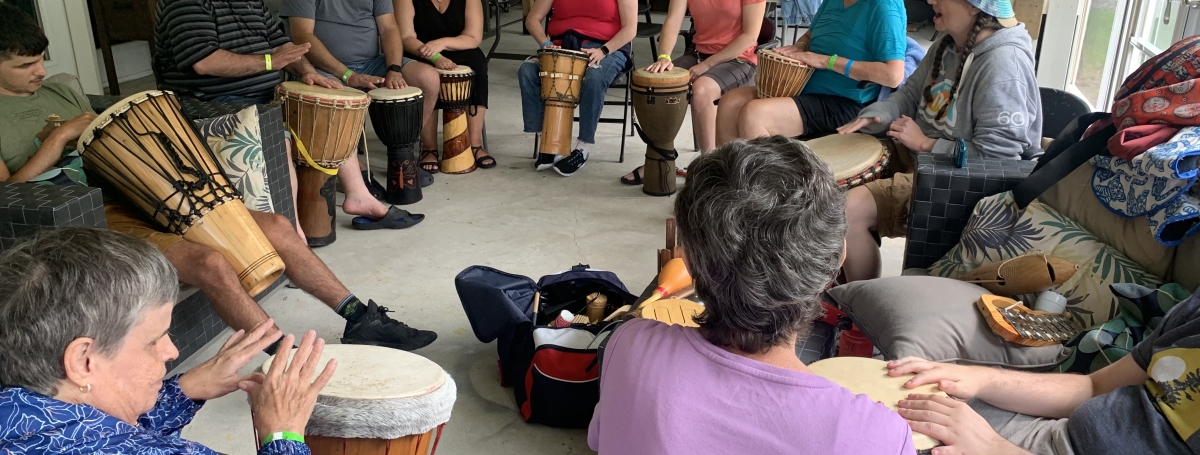 A group of adults are seated in a circle holding large drums in front of them.