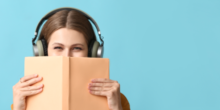 Une femme tient un livre devant son visage et porte des écouteurs.