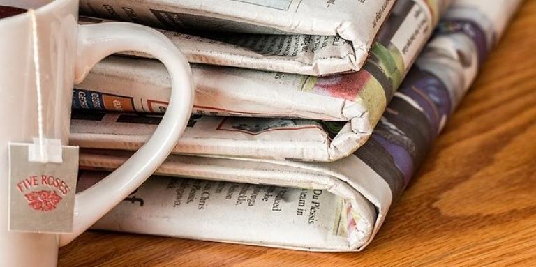 Three folded newspapers sits on a table next to a cup of tea.