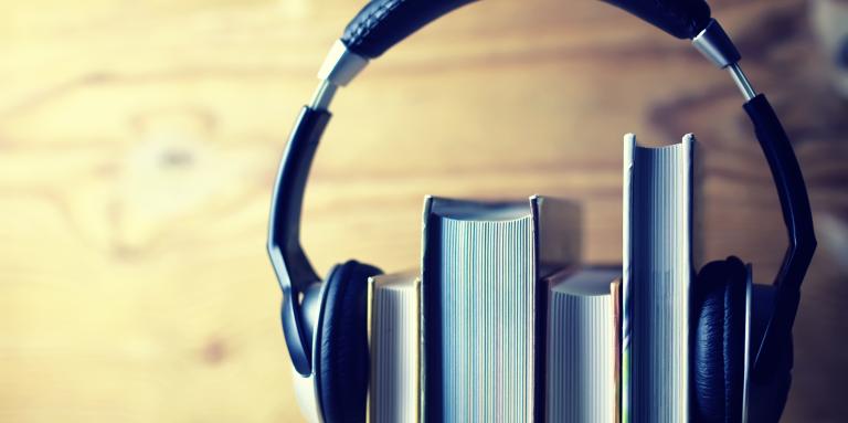 A stack of four books sits on a shelf. A pair of headphones sits on top of the books - holding them together.