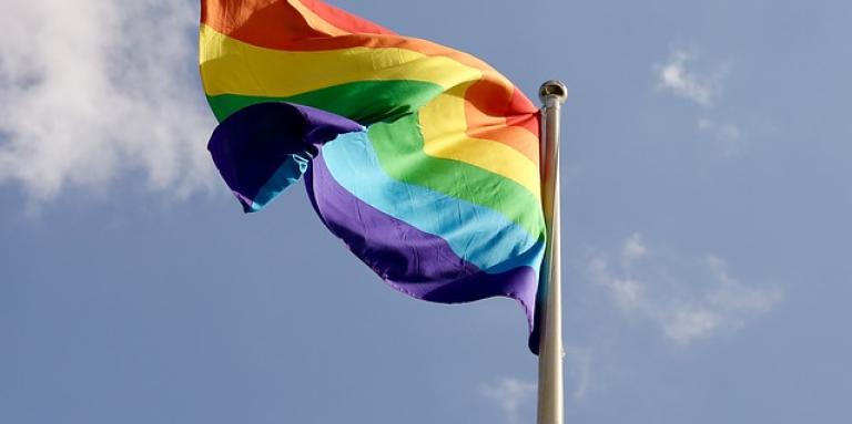 A colourful Pride flag waves in the wind on a flag post.