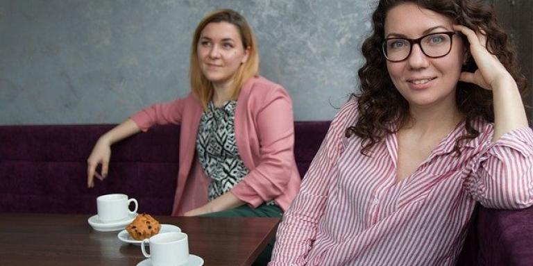 Two young women enjoy coffee at a cozy restaurant table.