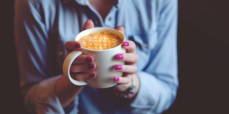 A woman's hands firmly grip a piping hot cup of coffee.