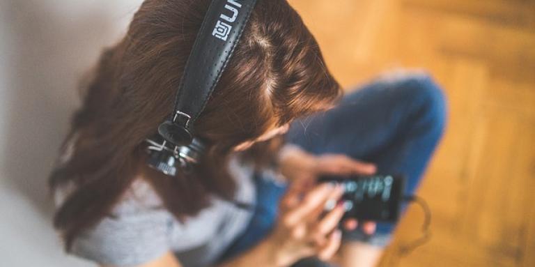 A young woman wearing headphones sits on the floor and listens to music on her iPhone.