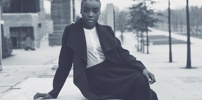 A young woman sits on a ledge outdoors. She is wearing a stylish business attire.