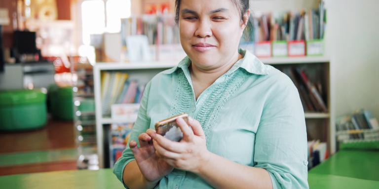 A young woman holds an iPhone in her left hand and double taps on the home screen.