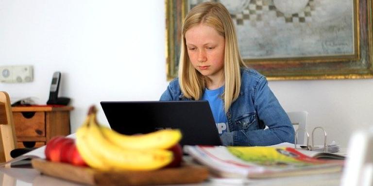 Home school. A young girl sits at a laptop computer at a kitchen island.