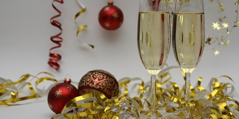 Two glasses of champagne sit on a table which is littered with Christmas bulbs, glitter and ribbon.