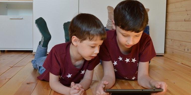 Two young brothers sit on their bedroom floor and interact with an iPad.