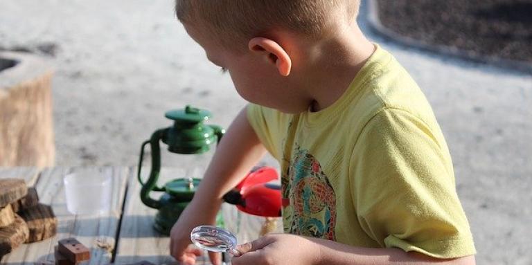 A young boy holds a magnifying glass and plays at a table.