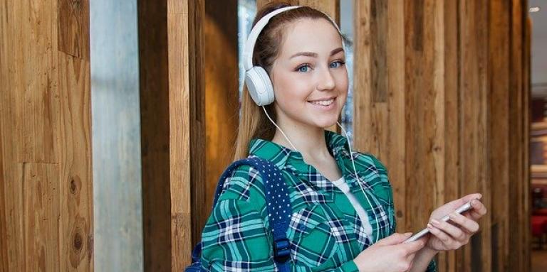 A young female student wears a backpack and headphones. The headphones are connected to her iPhone.