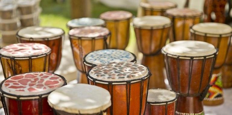 Multiple Djembe Drums sit outdoors on pavement ready to be played.