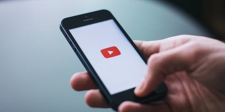 Une main tenant un smartphone avec le logo YouTube affiché sur l'écran.