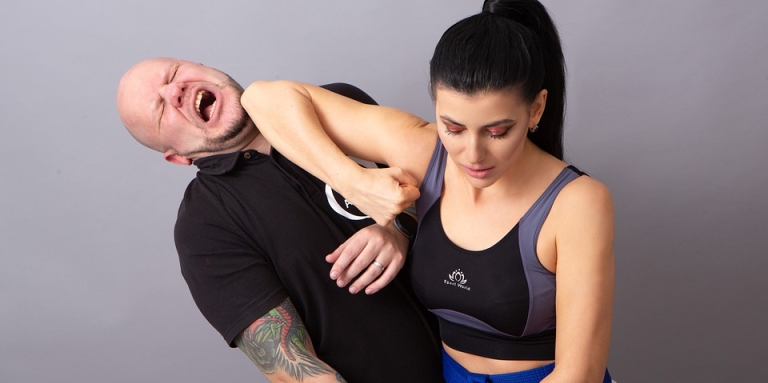 une femme en tenue sportif pratique l'auto-défense, son coude dans le visage d'un homme avec des tatouages