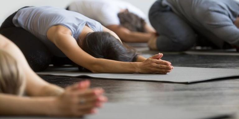 A yoga class. Three people kneel in a yoga position on their yoga mats.