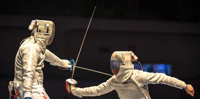 A fencing match. Two people wearing protective suits with their swords drawn.