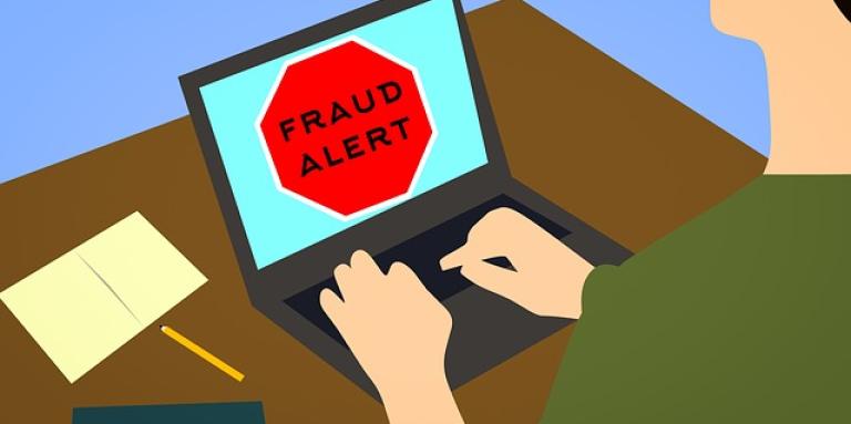 A cartoon illustration of a man sitting at a laptop computer. Laptop screen displays the text "Fraud alert!"