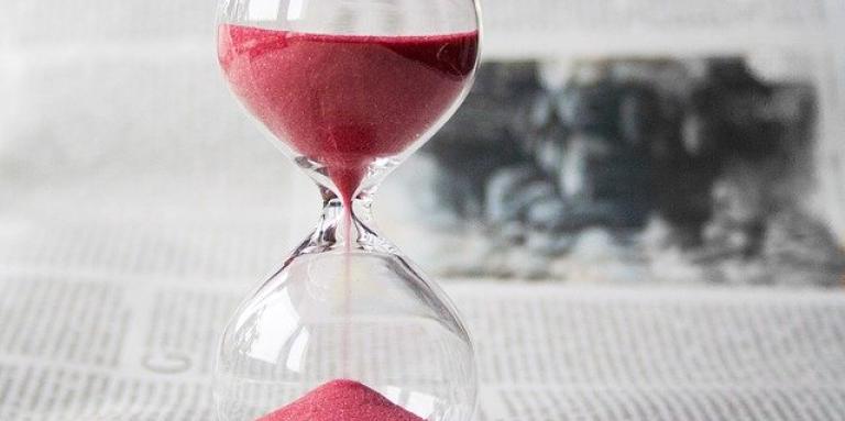 An hourglass distributes red sand.