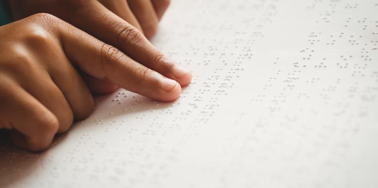 A child reads braille. Their hands move over a braille book.