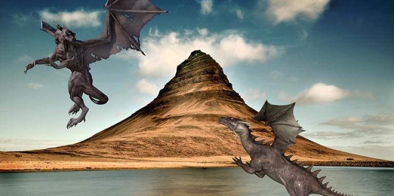 A computer graphic illustration of two dragons flying over a lake and mountain top.