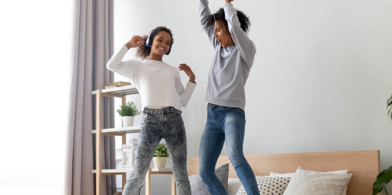 Two teenage girls singing and dancing on a bed.