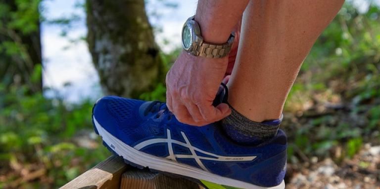 A man laces up a running shoe. His foot is resting on an elevated wooden post.