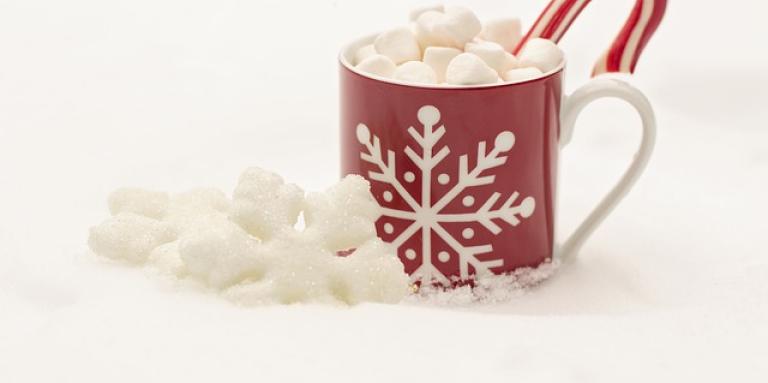 A cup of hot chocolate overflowing with marshmallows and a candy cane stick.