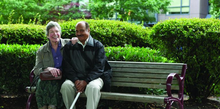 Man with white cane and woman sitting together on bench