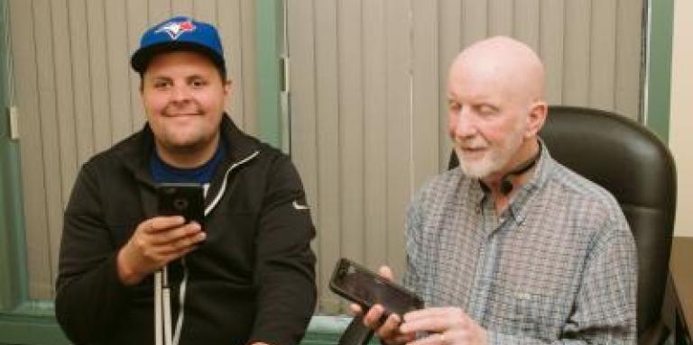 Two men smile and hold iPhones.