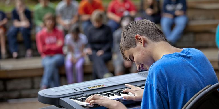 Teenage boy with sight loss playing keyboard for audience at talent show
