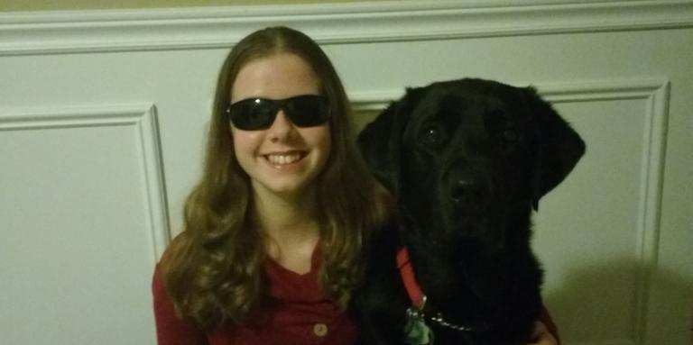 Teen girl with sight loss smiling and wrapping arm around her guide dog