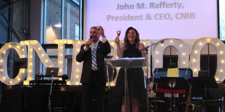 CEO and VP making a toast in front of CNIB 100 sign