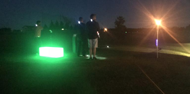 Golfers standing on the green with lights around them