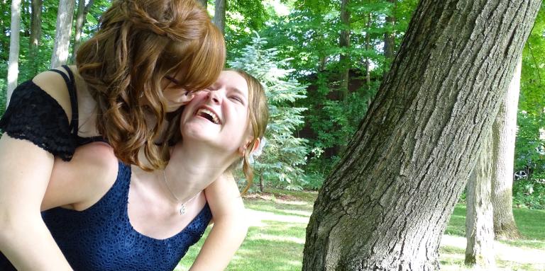 Emilee giving Hannah a piggy back and laughing while Hannah kisses her cheek.