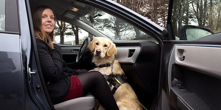 Une femme et son chien-guide, un Golden Retriever, assis dans le siège du passager d’une voiture.