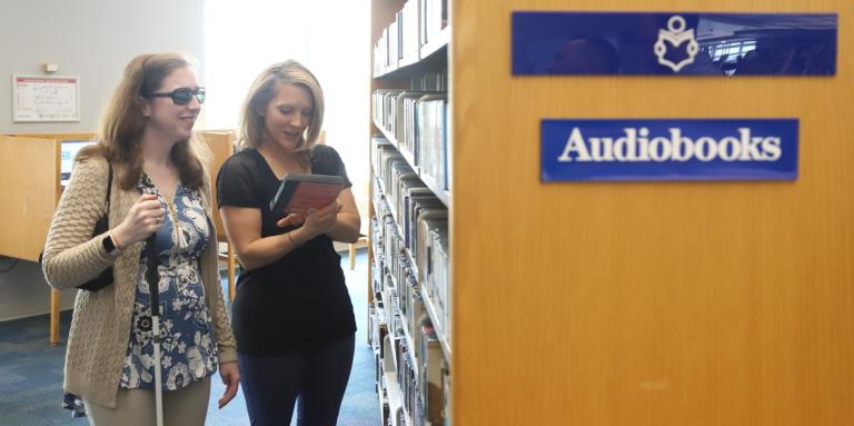 A CNIB volunteer reading title of an audio book to smiling client