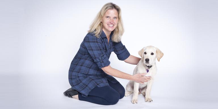 Un éleveur de chiots bénévole est assis à côté d'un jeune golden retriever lors d'une séance de photos professionnelle