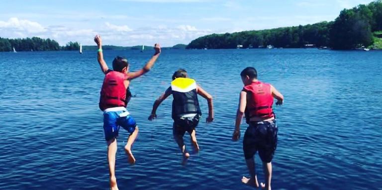 Trois jeunes garçons portent des gilets de sauvetage et sautent du quai dans le lac à INCA Lake Joe.