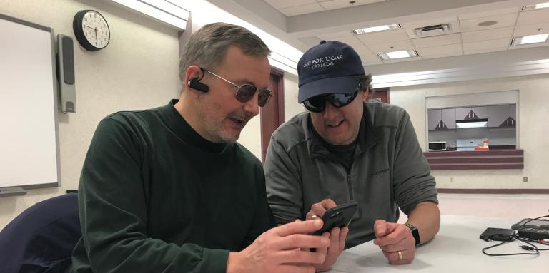 Lloyd Buckler, sitting down at a table helping someone learn how to navigate their iPhone. 