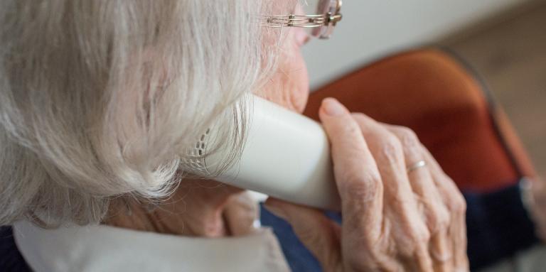 An elderly woman holds a landline telephone to her ear.