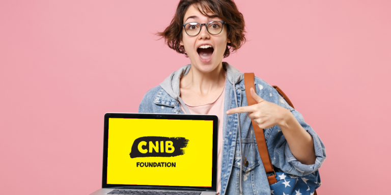 A young teenage girl excitedly holds a laptop monitor displaying the CNIB Foundation logo. She is pointing to the screen with her left hand.