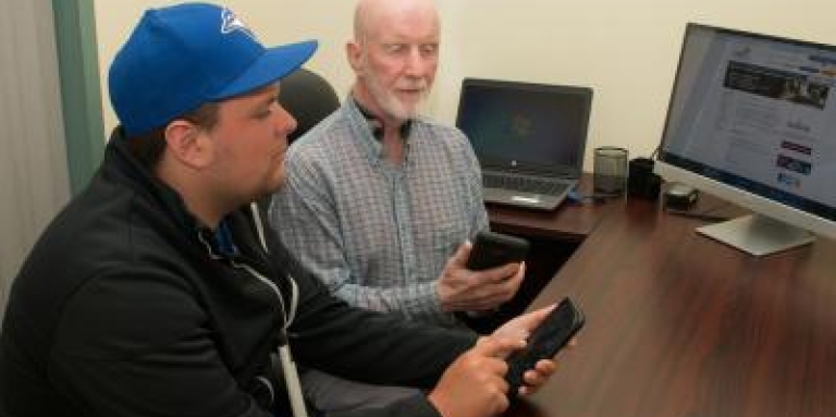 Deux hommes tiennent des iPhones devant un ordinateur.