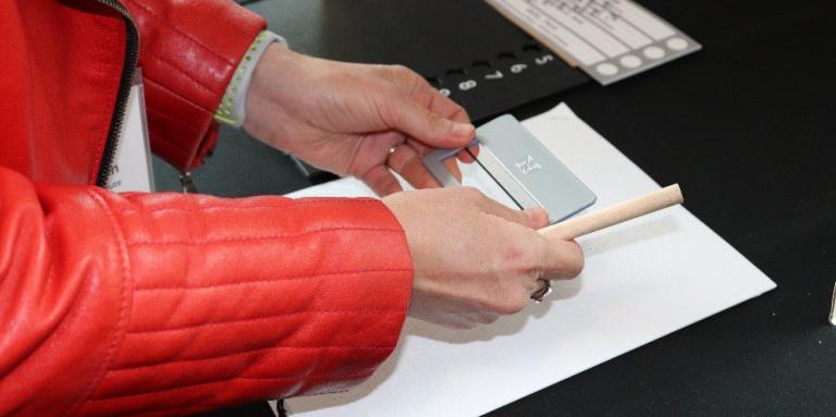 A woman holds a signature guide over a braille document. A tactile voting template is beside her.