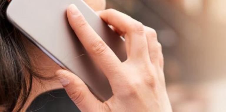 A hand holds an iPhone to a woman's ear.