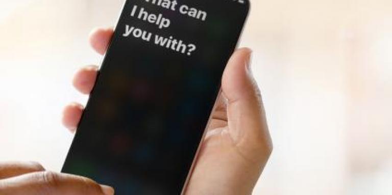 An iPhone 11 screen displays magnified text that reads "What I can I help you with?"