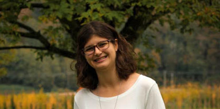 Amy Verwoerd, standing outside with a lush field in the background, smiling for the camera