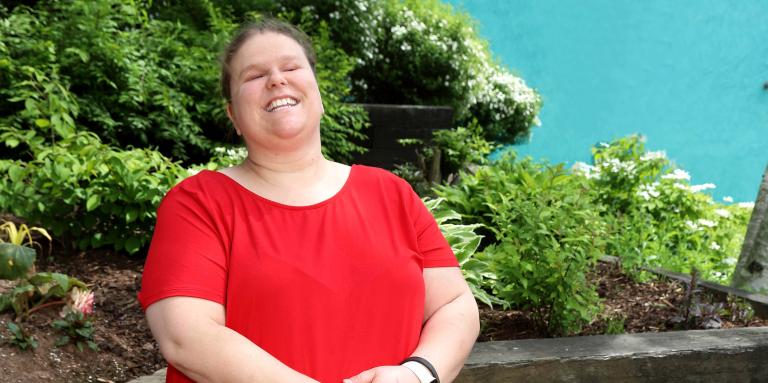 Jennifer MacNeil, debout dehors par une journée ensoleillée, souriant pour la caméra avec Lenny, son chien-guide.