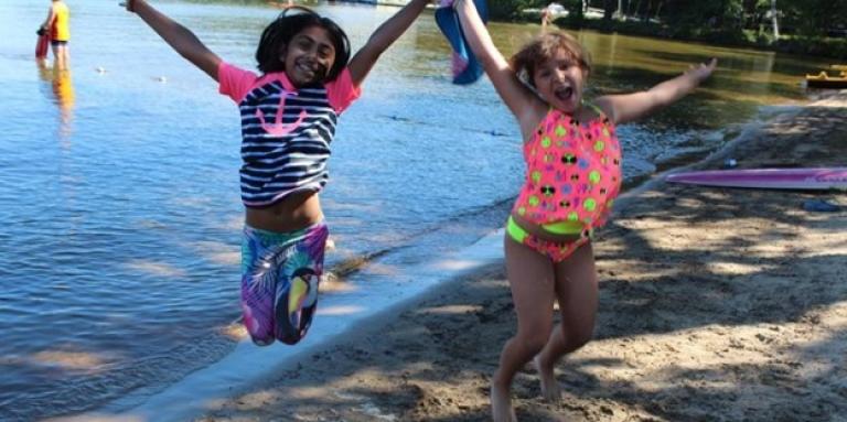 Deux jeunes filles souriantes en maillot de bain sautillant sur la plage.