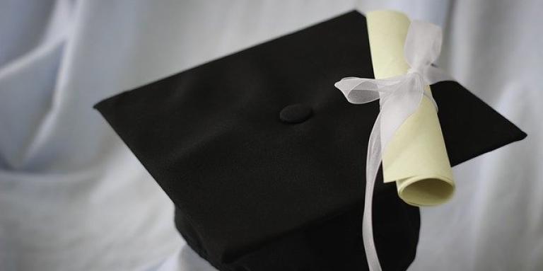 Un diplôme roulé sur une toque devant un arrière plan en tissu blanc.